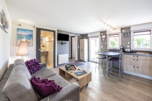 A modern living room with a grey sofa, purple cushions, a wooden coffee table, and a kitchen area with a bar stool. - Gîte le rêve: Between Lake and Mountains, Near Aix-les-Bains and Savoie Grand Revard (Viviers du Lac)