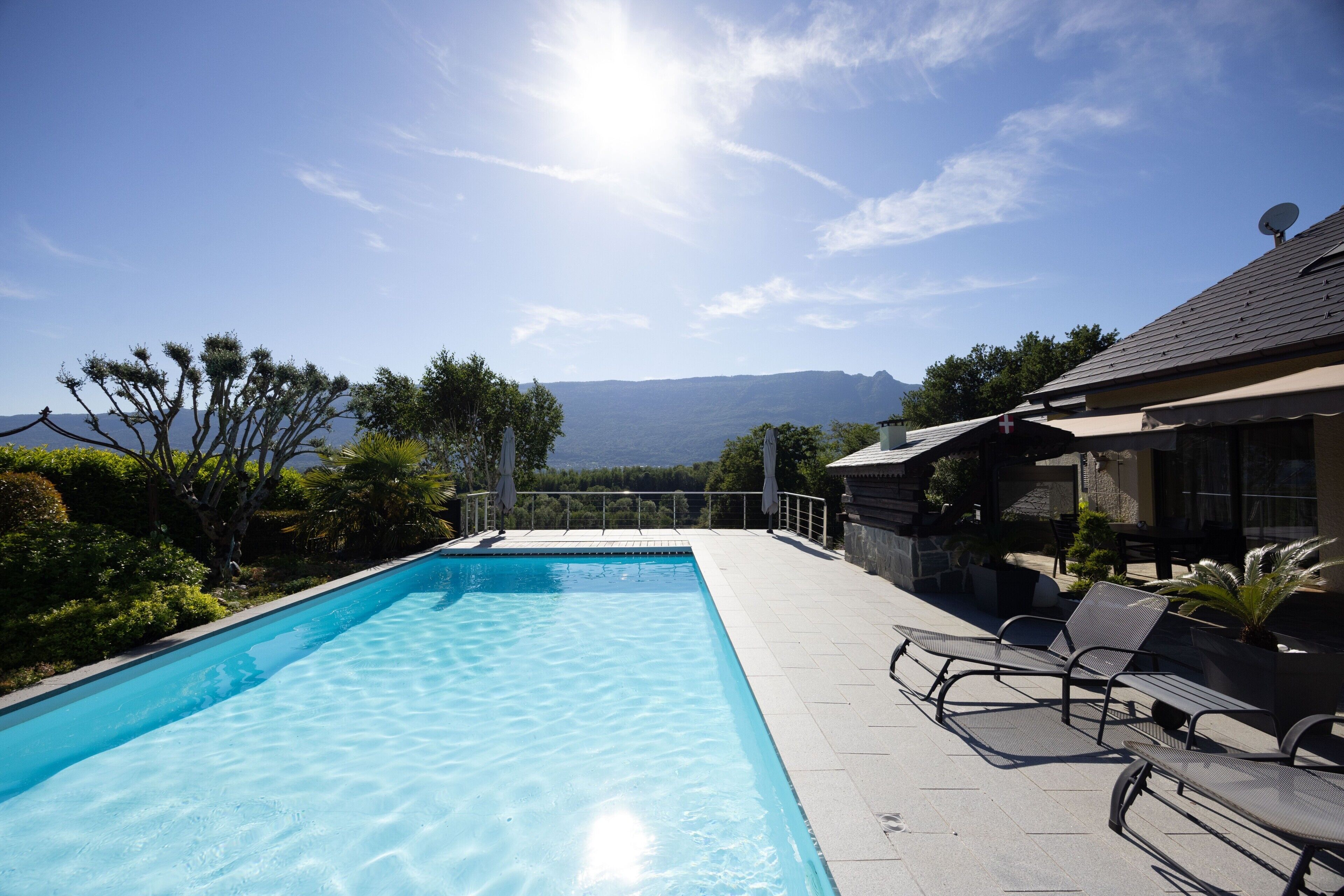 A swimming pool with clear water, surrounded by a patio area with chairs and a view of mountains in the background.