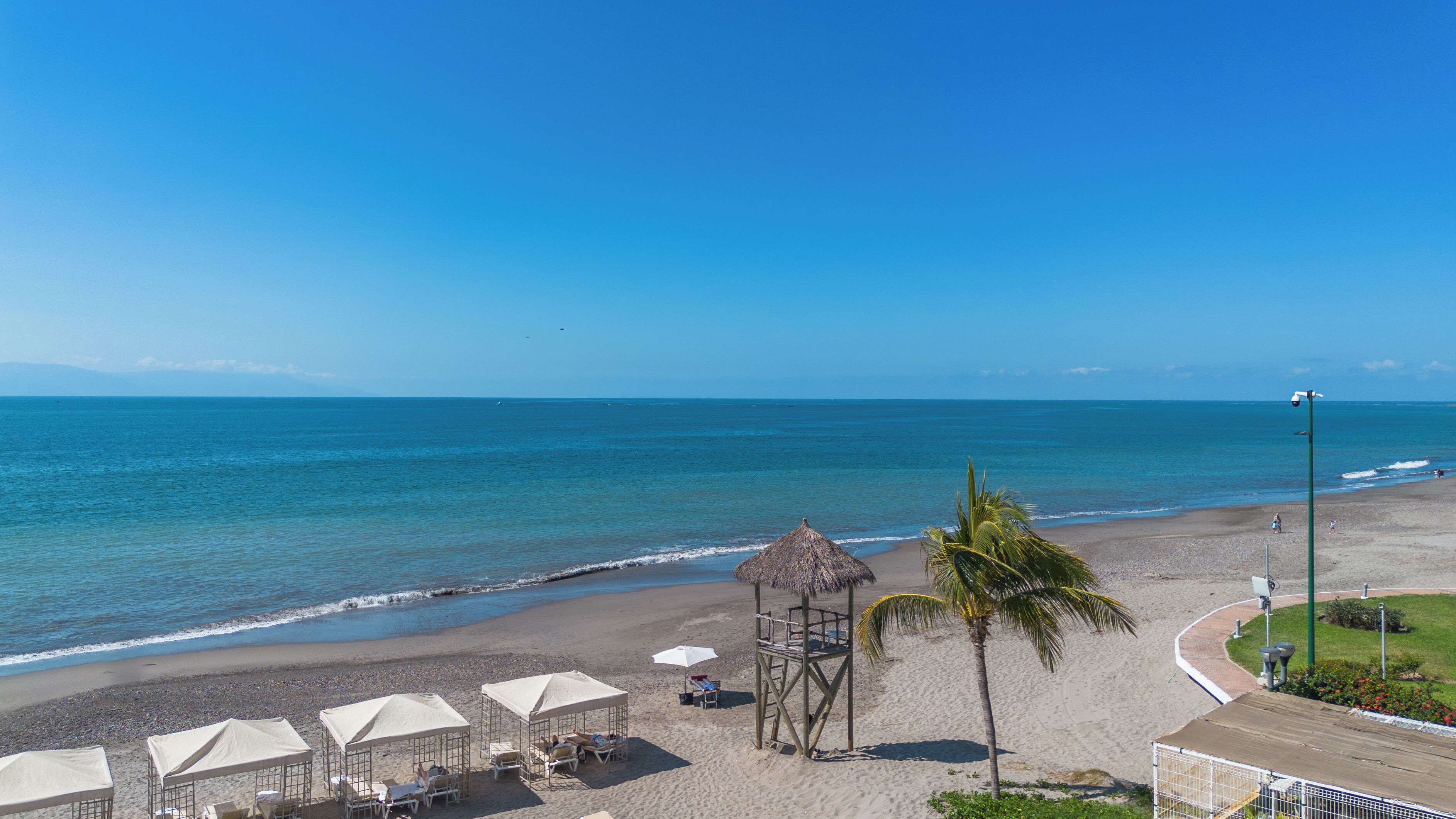 Una playa con sombrillas, una cabaña de techo de paja y una torre de salvavidas.
