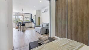 A modern hotel room with a large bed, a sofa, a dining area, and a view through a glass door. - Apartment 'Machadinho' with Private Pool, Wi-Fi and Air Conditioning (Albufeira)