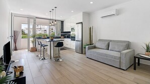 A modern kitchen with a dining area, a grey sofa, and a TV on a stand. - Apartment 'Machadinho' with Private Pool, Wi-Fi and Air Conditioning (Albufeira)