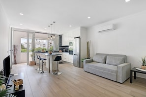 A modern kitchen with a dining area, a grey sofa, and a TV on a stand. - Apartment 'Machadinho' with Private Pool, Wi-Fi and Air Conditioning (Albufeira)