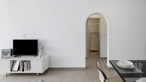 A modern living room with a flat-screen TV, books, and a small plant on a white cabinet. - Casa machadinho - Albufeira (Albufeira)