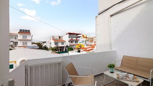 A balcony with a chair, a small table with a plant, and a tray with cups and a book. - Casa machadinho - Albufeira (Albufeira)