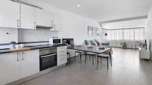 A modern kitchen with white cabinets, a microwave, and a dining area with a table and chairs. - Casa machadinho - Albufeira (Albufeira)