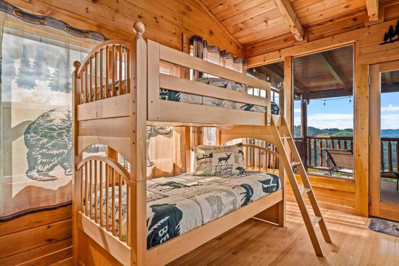 Ein Holzbett mit Etagen und einer Leiter, ein Fenster mit einer Waldfresco sowie ein Blick ins Freie.