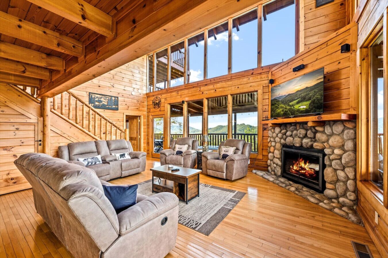 A spacious living room with a fireplace, wooden floors, and a large window overlooking a scenic view.
