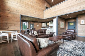 A spacious living area with leather sofas and armchairs, a dining table, and a kitchen in the background. - New! Luxe Pool Cabin w/MTN Views*Hot Tub*Fire pit (Sevierville)