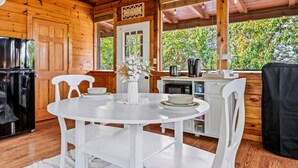 L’intérieur d’un chalet en bois comprend une table à manger, des chaises, un réfrigérateur, une machine à café et offre une vue sur la verdure environnante.