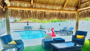 Ein Poolbereich mit Liegestühlen, einem Flamingo-Schwimmpfleg und einer überdachten Laube mit Reetdach.