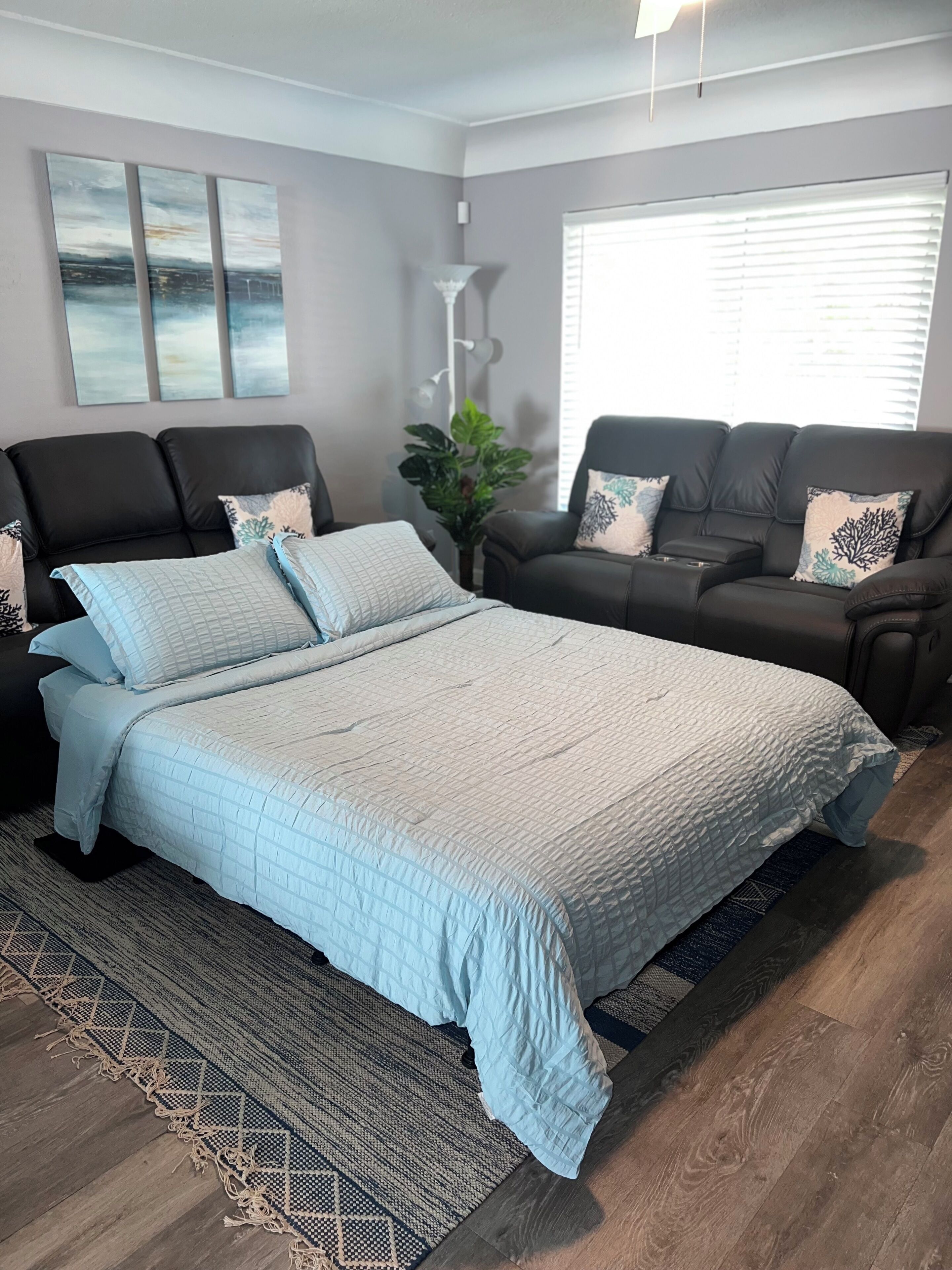 A bedroom with a large bed, two black leather sofas, a floor lamp, and a potted plant.