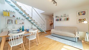Um espaço de estar moderno com área de jantar, sofá e escada com guarda-corrimão de vidro.