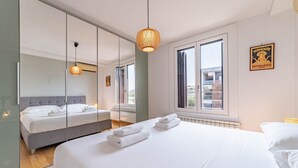 Quarto de hotel moderno com uma cama grande, um espelho, uma janela com vista e um candeeiro suspenso.