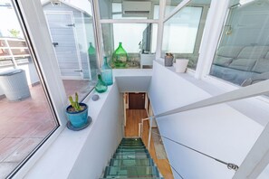 Een modern interieur met een glazen trap, een kleine potplant en een raam met uitzicht op een patio.