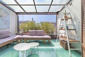 A sunroom with a glass floor, a cushioned seating area, and a ladder with plants. - [10' Navigli] Penthouse with Panoramic View Milan (Milan)