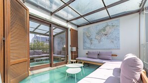Quarto moderno com teto de vidro, um grande mapa-múndi na parede, sofá, mesa pequena e porta de vidro deslizante para área externa.