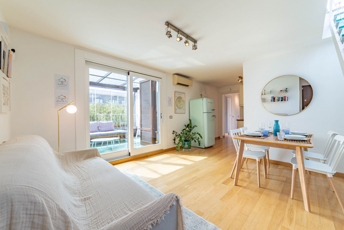 Ein modernes Zimmer mit einem Bett, einem Esstisch mit Stühlen, einer kleinen Küchenzeile und einer Glastür, die zu einem Außenbereich führt.