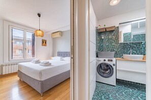 A bedroom with a bed, a washing machine, and a bathroom with a sink and tiled walls. - [10' Navigli] Penthouse with Panoramic View Milan (Milan)