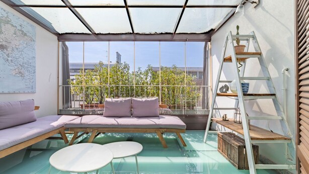 Uma sala de sol com piso de vidro, área de estar acolchoada e escada com plantas.