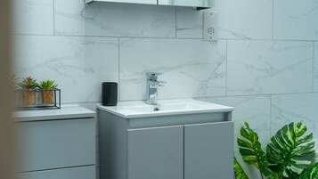 Un baño moderno con un lavabo de mármol blanco, armarios grises y una planta pequeña en la encimera.