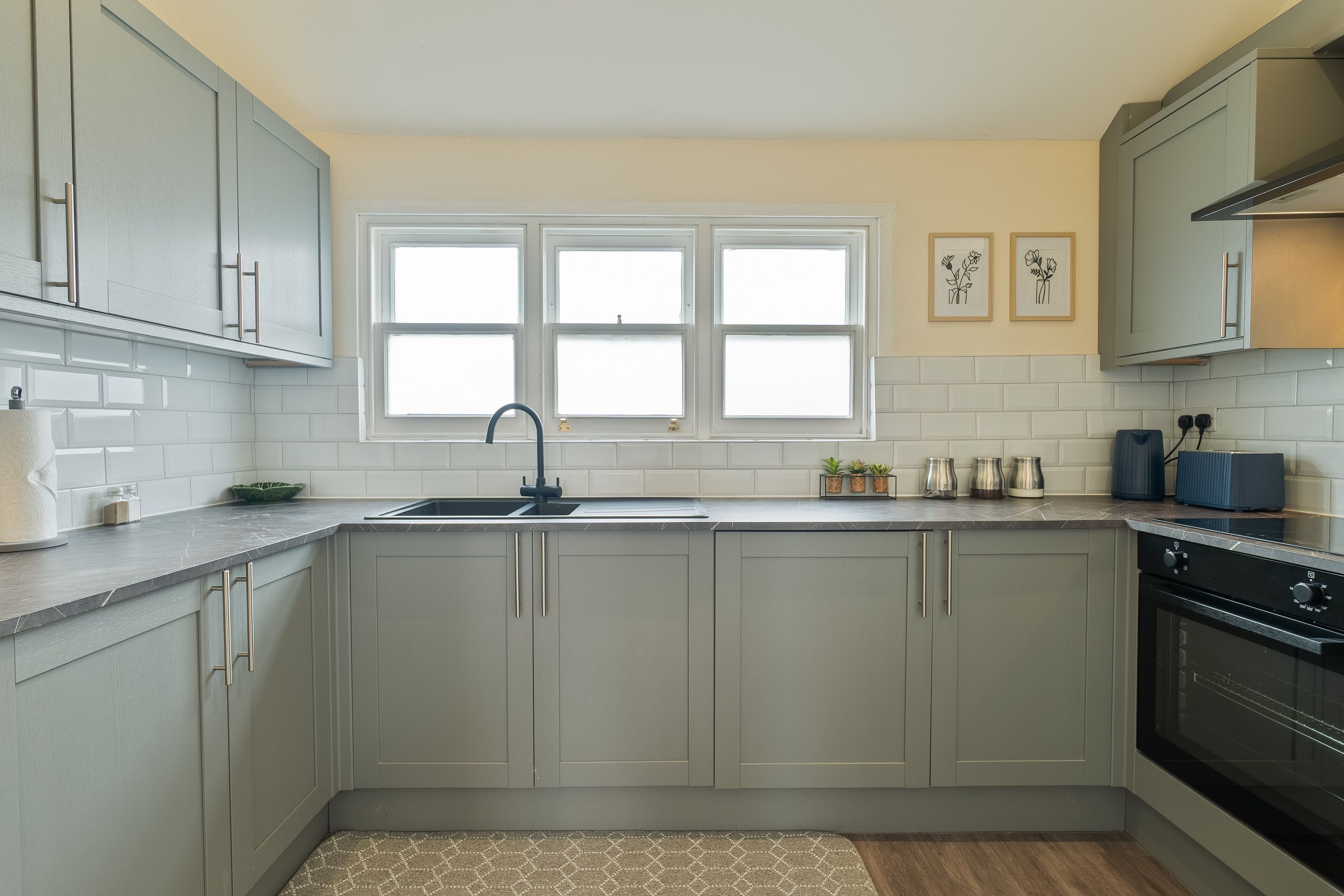 A kitchen with grey cabinets, a black sink, and a window above the countertop.