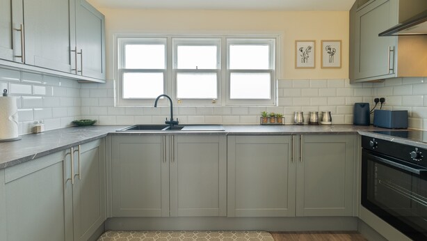 A kitchen with grey cabinets, a black sink, and a window above the countertop. - Unique Rooftop Retreat | City View | Sleeps 4 (Kent)