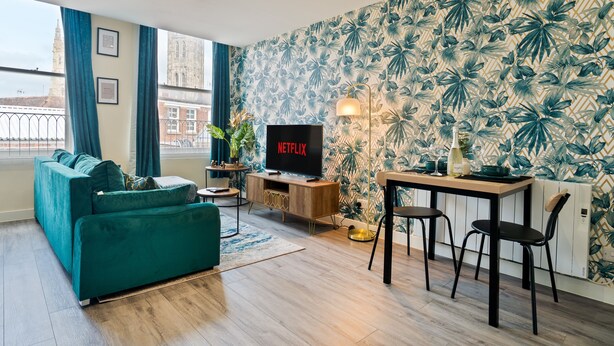 A modern living room with a sofa, a TV, a table with chairs, and a patterned wall. - Stylish City Centre getaway w/ Cathedral Views (Kent)
