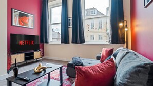 Un salon moderne avec un téléviseur à écran plat affichant le logo « NETFLIX », un canapé, une table basse et une fenêtre avec des rideaux.