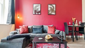 Un salon moderne avec un canapé gris, des coussins rouges, une table basse et un coin repas comprenant des chaises et une table.
