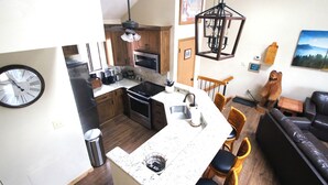Cocina compacta con microondas, estufa y lavamanos. Hay una zona de comedor con mesa y sillas. Un reloj está colgado en la pared.