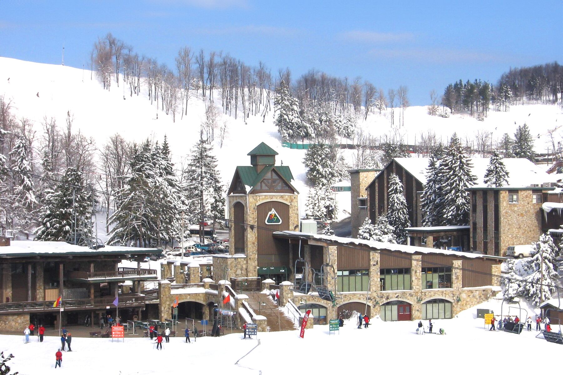 A ski resort with a stone building featuring a clock tower, ski lifts, and a snowy landscape.