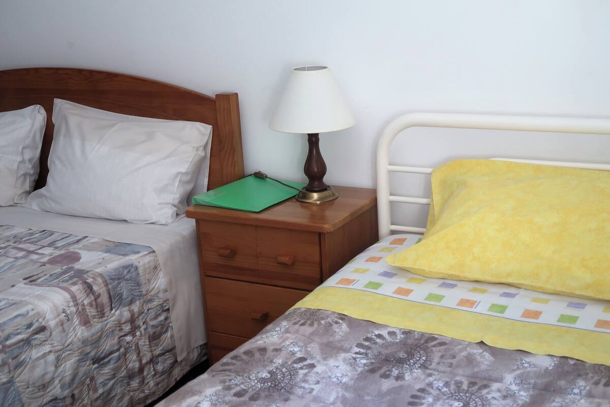 A bedroom with two beds, a nightstand with a lamp, and a green folder on the nightstand.
