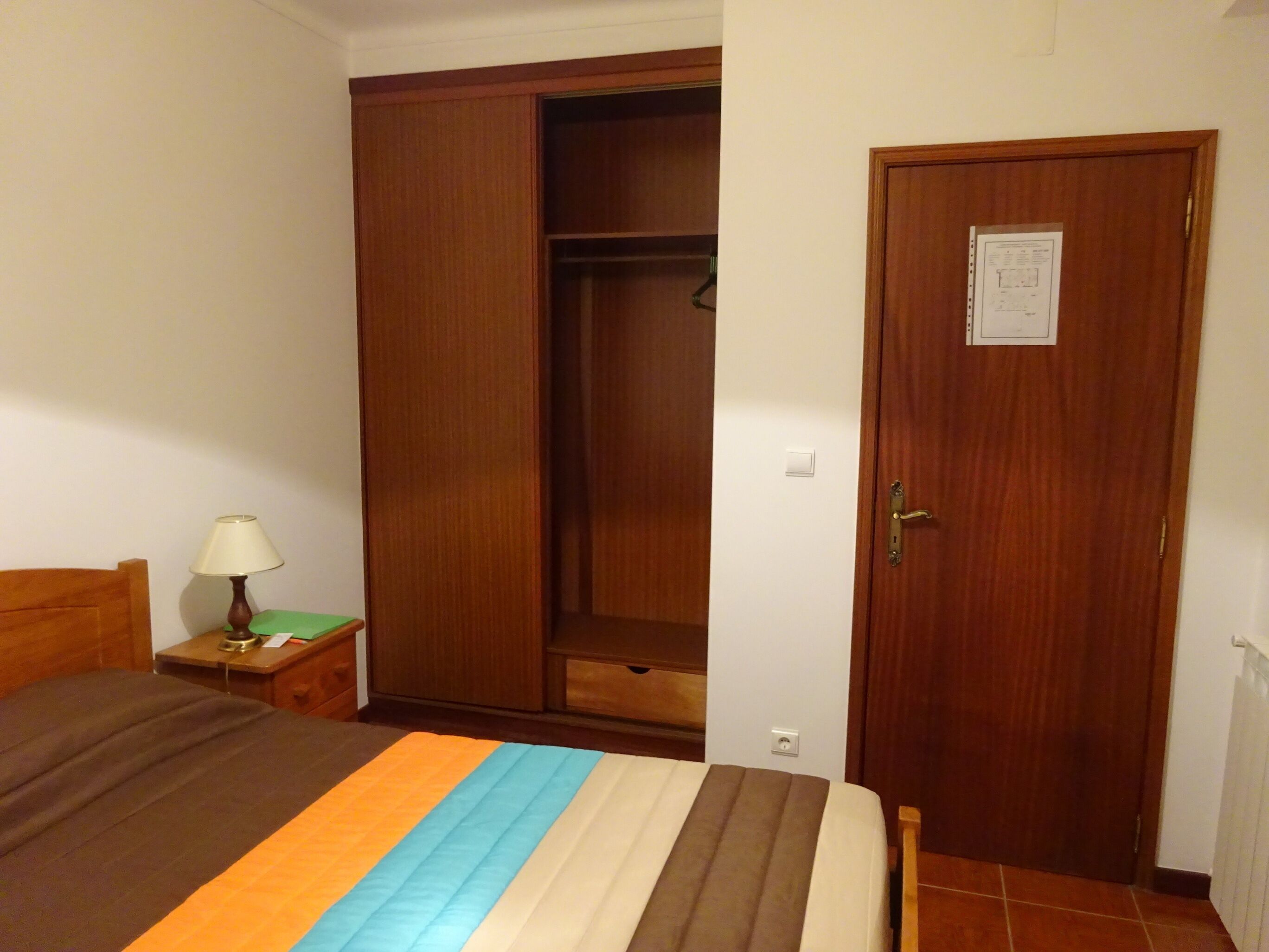 Une chambre à coucher comprenant un lit, une table de chevet, une lampe, une armoire en bois et une porte avec une serrure.