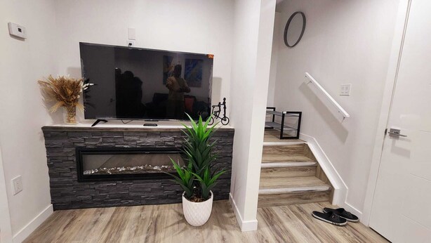 Een moderne woonkamer met een stenen open haard, een flatscreen televisie, een potplant en een trap naar een hoger gelegen verdieping.