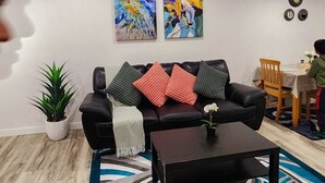 Een moderne woonkamer met een leren zwarte bank, een salontafel en abstracte schilderijen aan de muur.