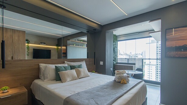 A modern bedroom with a large bed, a flat-screen TV, a city view, and a balcony with a chair. - Elegance and Comfort - Close to Allianz Parque Sp-p2202b (São Paulo)