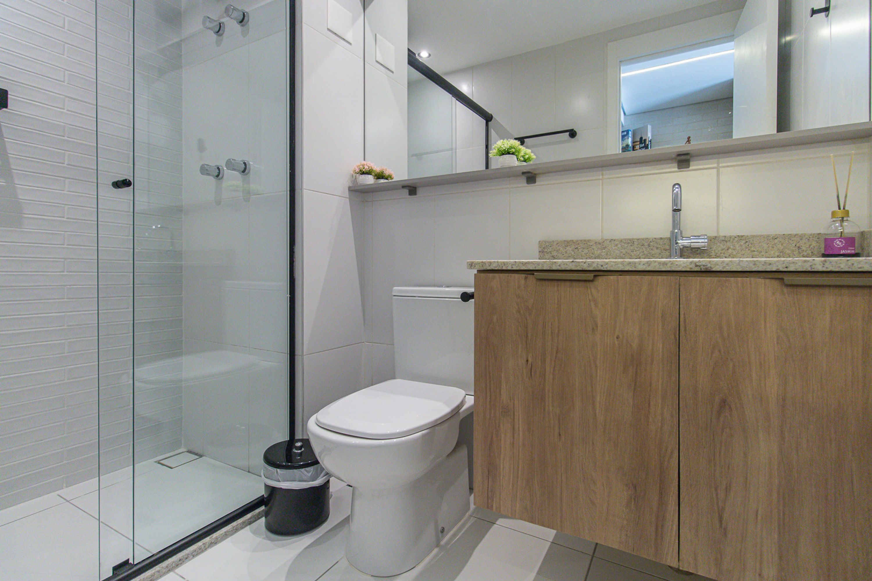 Een moderne badkamer met een douchecabine van glas, een wit toilet en een houten wastafelmeubel met een granieten werkblad.