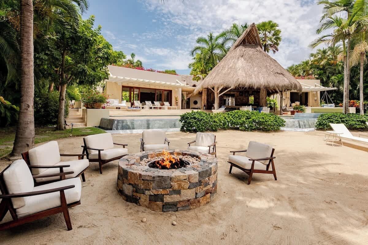 Resort com estrutura de telhado de palha, piscina, espreguiçadeiras e lareira.