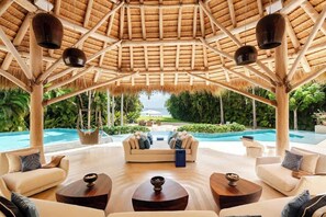 Un espace de détente extérieur abrité, doté d’une piscine, de canapés et de tables, et surmonté d’une structure à toit de chaume.