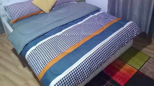 A neatly made bed with a patterned bedspread and pillows, a bedside table with a lamp, and two framed artworks on the wall. - Home Stay In Accra, Travellers With Kids Are Welcomed. 5 mins Walk Away To Beach (Accra)