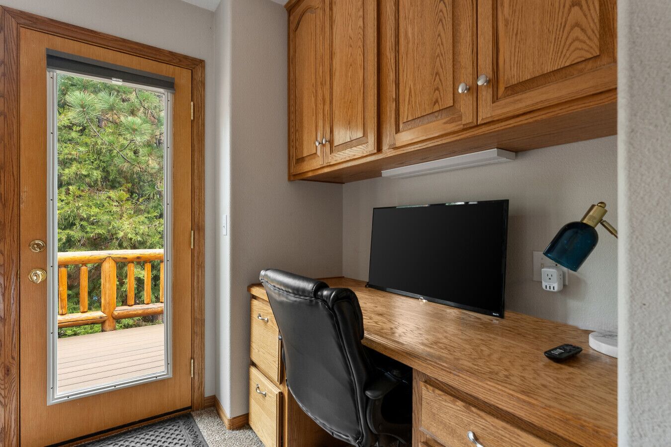Een kamer met een houten bureau, een zwarte stoel, een televisie en uitzicht op een balkon met houten leuning.