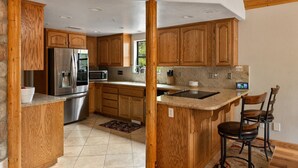 Eine Küche mit Holzausstattung, Edelstahlgeräten, einer Arbeitsplatte aus Granit und einer Bar mit Hockern.