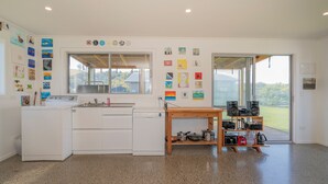 Una cocina moderna con electrodomésticos blancos, una mesa de madera con altavoces y vistas a través de la puerta de cristal.