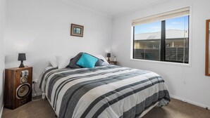 Une chambre à coucher avec un lit, un haut-parleur en bois, une fenêtre et un tableau encadré au mur.