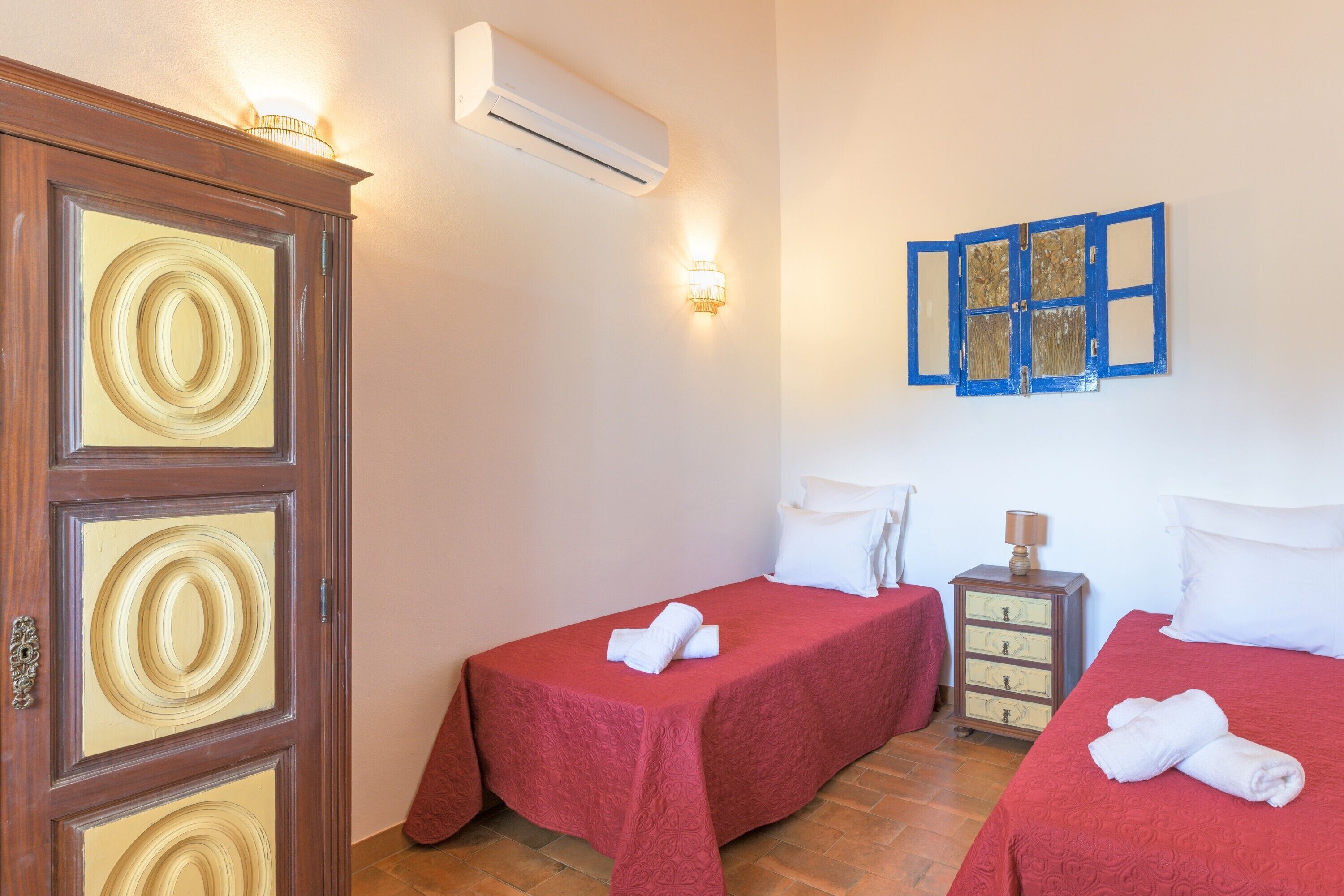 Une chambre d’hôtel avec deux lits, une armoire, un climatiseur, une lampe fixée au mur et une petite table de chevet.