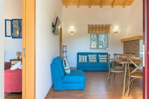 Ein Zimmer mit einem blauen Sofa, einem Esstisch mit Stühlen, einem Kamin und einer Holzbalkendecke.