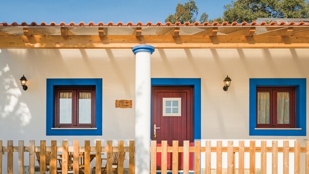 Un bâtiment à deux étages, doté d’une clôture en bois, d’une porte rouge et d’une fenêtre à cadre bleu.