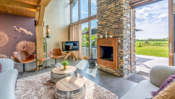 A modern living room with a stone fireplace, large windows, and a cozy seating area. - Attractive and Modern 6-person Holiday Villa (De Koog)