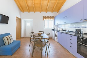 Uma cozinha com máquina de lavar roupa, uma sala de jantar com cadeiras e mesa, e um sofá azul.