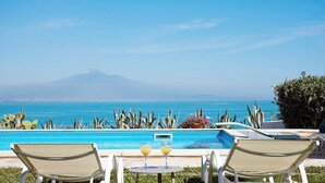 A poolside view with two lounge chairs, a table with drinks, and a view of the ocean and a mountain in the distance. - Villa Saracena - Seven Bedroom Villa, Sleeps 14 (Costa Saracena - Castelluccio)